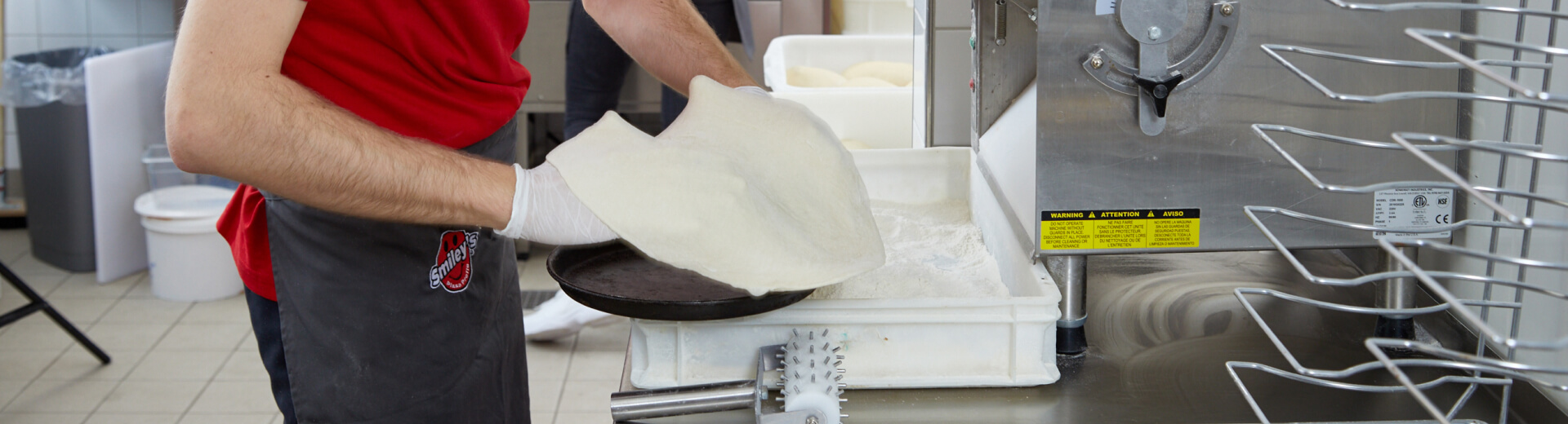 Smiley’s Mitarbeiter legt frischen Pizzateig in ein Backblech