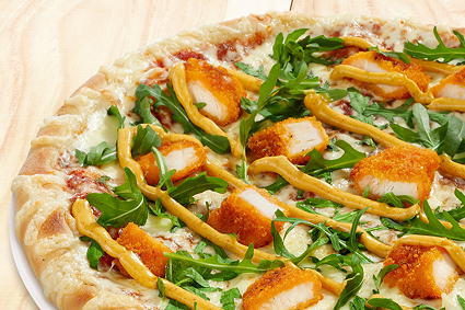 Nahaufnahme einer Pizza mit knusprigem Hähnchen, frischem Rucola und gelber Soße auf einem dünnen Boden mit Käserand. Serviert auf weißem Teller vor hellem Holzhintergrund