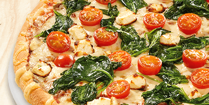 Pizza mit frischem Spinat, halbierten Cherrytomaten und kleinen Käsewürfeln