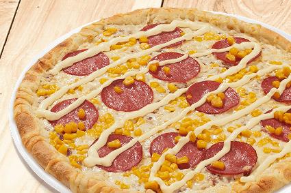 Pizza mit Salami, Mais und Streifen aus heller Sauce auf Holzuntergrund