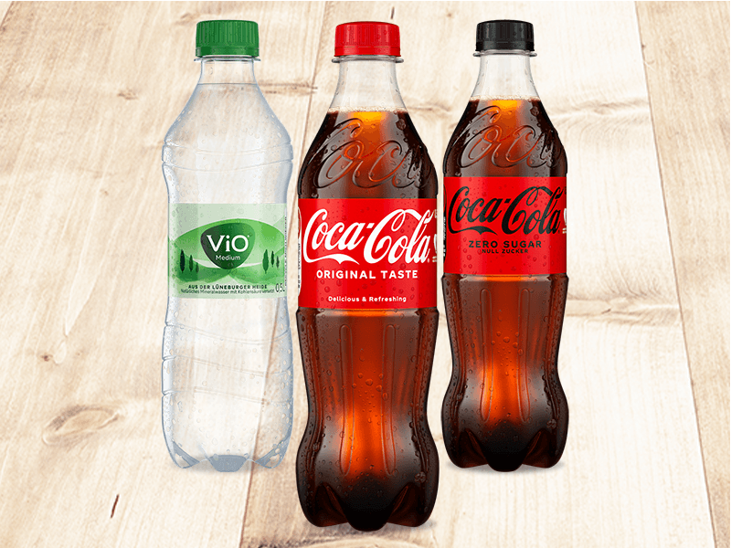 Drei fritz-Getränkeflaschen: fritz-limo Orange, fritz-kola Original und fritz-kola Super Zero auf hellem Holzhintergrund.