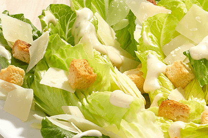 Caesar-Salat auf weißem Teller: Römersalatherzen, knusprige Croutons, Parmesanspäne und cremiges Dressing