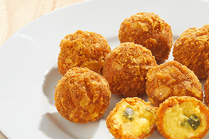 Knusprig panierte Käsebällchen mit Gurkenstücken auf weißem Teller